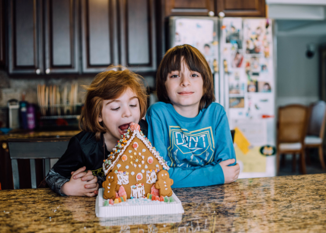 School-aged children on holiday break with a ginger bread house